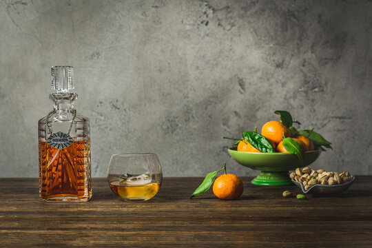Bourbon in vintage decanter and rocks glass with bowl of mandarin oranges ond bowl of pistachios