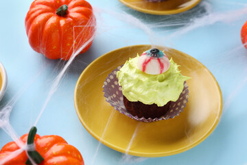 Plate with delicious Halloween cupcake and pumpkins on blue background, closeup