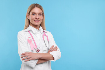 Doctor with pink ribbon and stethoscope on light blue background, space for text. Breast cancer...