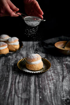 Semlor Buns on Wood Backdrop with icing sugar on tray with hands