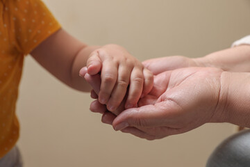 Woman holding hands with her granddaughter on beige background, closeup