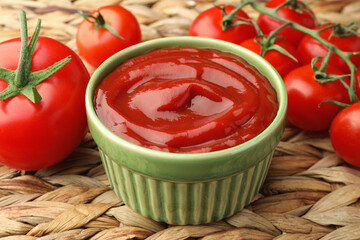 Bowl of tasty ketchup and tomatoes on wicker mat, closeup