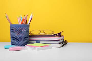 Different school stationery and glasses on white table against yellow background, space for text. Back to school