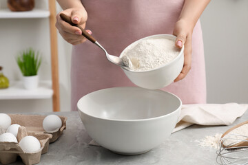 Preparing tasty baklava. Woman putting flour into bowl at light grey marble table, closeup