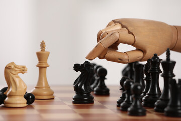 Robot moving chess piece on board against light background, closeup. Wooden hand representing artificial intelligence