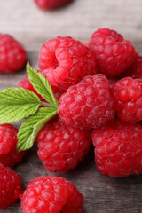 Tasty ripe raspberries and green leaves on wooden table, closeup