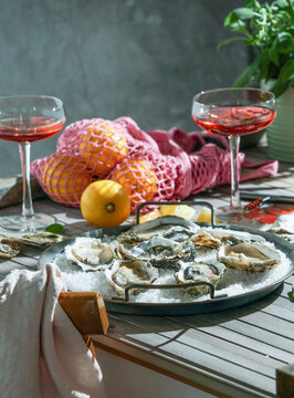 Fresh oysters with lemon on a metal tray on a wooden table. Hot summer day, picnic outside