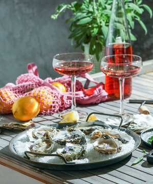 Fresh oysters with lemon on a metal tray on a wooden table. Hot summer day, picnic outside