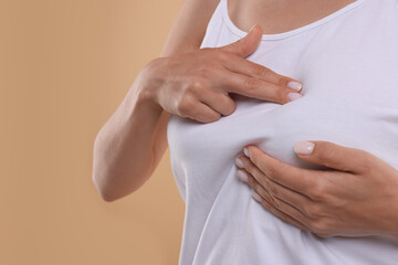 Woman doing breast self-examination on light brown background, closeup. Space for text