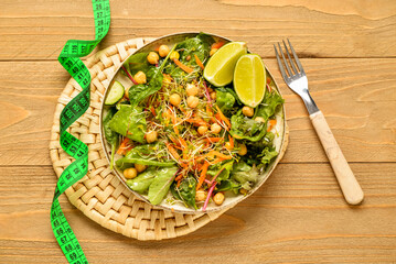 Plate with fresh salad and measure tape on wooden background. Diet concept