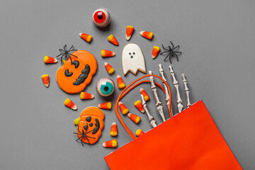 Shopping bag with tasty candy corns, cookies for Halloween and skeleton hand on grey background