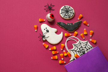 Shopping bag with tasty candy corns and cookies for Halloween on pink background