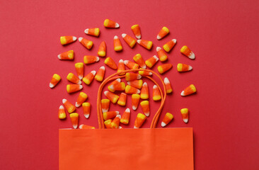 Shopping bag with tasty Halloween candy corns on red background