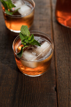 Peach iced tea in a small tumbler with ice cubes and fresh mint leaves.