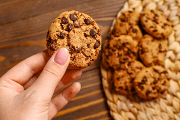 Woman holding tasty cookie with chocolate chips on wooden background