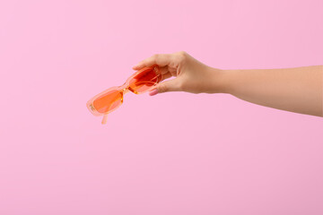Woman holding stylish sunglasses on pink background