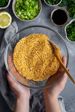Hands holding a bowl of soaked fine bulgur wheat, chopped herbs, half lemon and pomegranate molasses accompany.