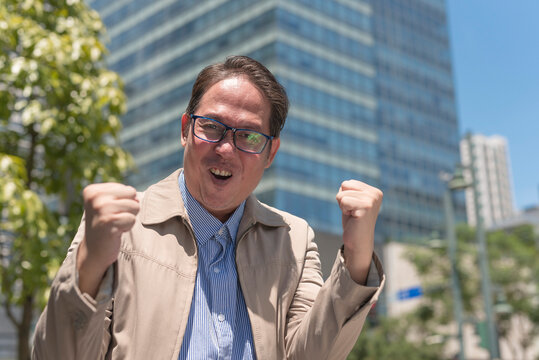 An elated middle aged man roars success, looking at the camera. Reacting outside after being promoted to a senior managerial role. Outdoor city scene.