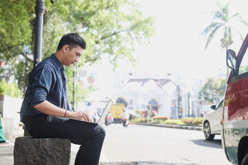 Serious young Asian business man  using laptop outside the office  