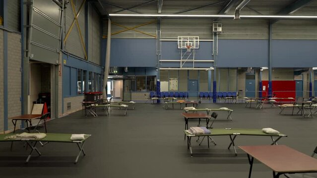 Refugee shelter on basket ball sports hall bed and table line up dolly shot