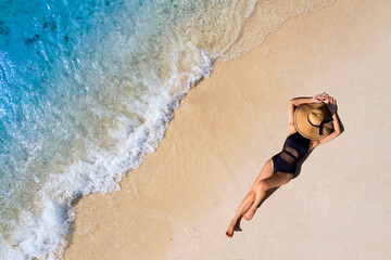 Aerial view of beautiful young woman in black swimsuit lying on sandy beach near blue sea with...