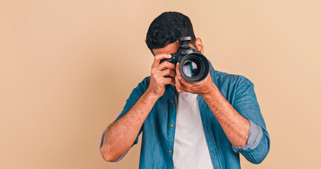 Young photographer standing and holding camera on brown background.