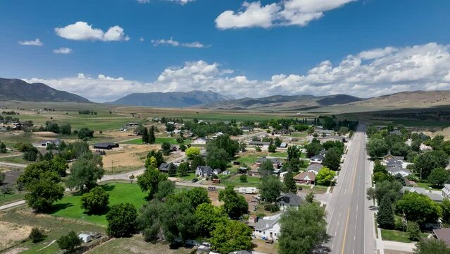 Aerial rural city homes mountain valley summer Utah 1. Farming community agricultural economy. Spring summer weather mountain valley green agriculture field. Homes, barns, buildings.