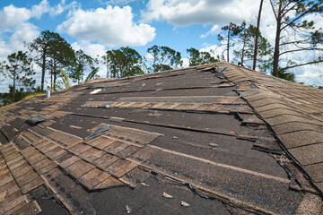 Damaged house roof with missing shingles after hurricane Ian in Florida. Consequences of natural...