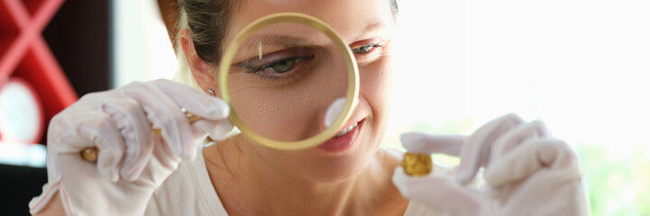 Woman numismatist looking through magnifying glass at gold coin close up.