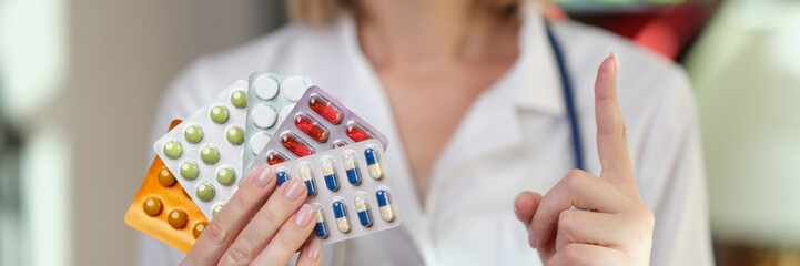 Female pharmacist holds packs of medical pills and points her finger up.