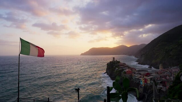 The Italian flag is blowing in the wind at sunset at the Mediterranean seaside village of Vernazza, Cinque Terre, Italy.