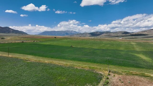 Aerial rural farm fields tractor agriculture mountain valley summ. Farming community agricultural economy. Summer harvesting of alfalfa hay agriculture. Tractor equipment, Seasonal rural farm harvest.