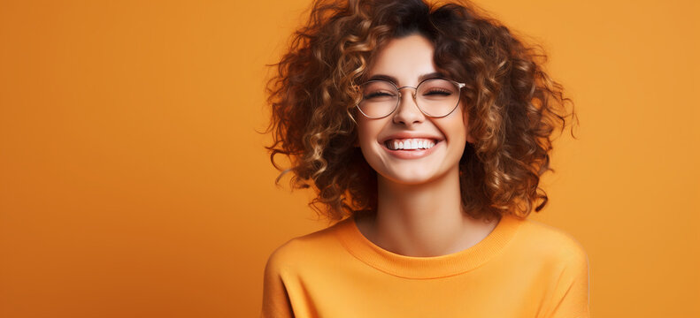 portrait of a young adult woman smiling against orange background.