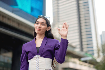 A lovely lady standing outside in a purple suit and white corset is gesturing 'hi' while smiling at...