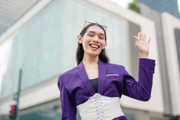 A lovely lady standing outside in a purple suit and white corset is gesturing 'hi' while widely...