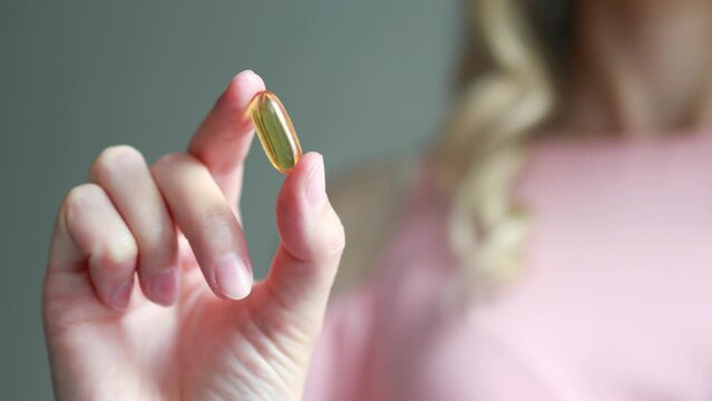 A woman holds in her hand a capsule of dietary supplement with fish oil or omega 3, vitamin A, E, D. Healthy lifestyle.