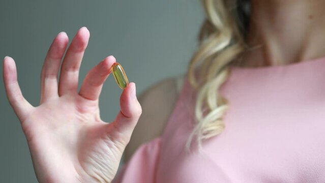 A woman holds a yellow capsule with dietary supplement in her hand. Omega 3, fish oil, vitamin D3