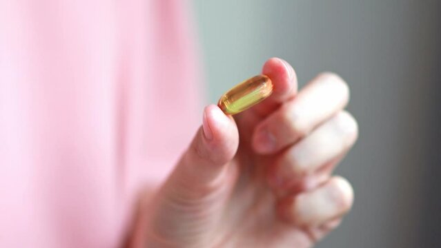 Close-up woman holds in her hand a capsule of dietary supplement with fish oil or omega 3, vitamin A, E, D, and drinks it with a glass of water.
