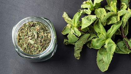 Dried peppermint in a glass jar and a bunch of fresh mint, medicine herb on black background, top...