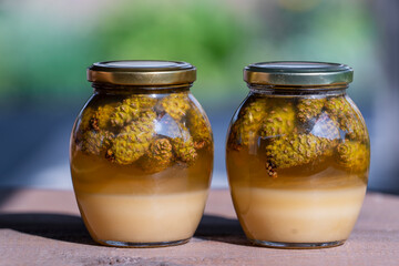 Two glass jars of fresh honey with pine cones on a wooden table, closeup