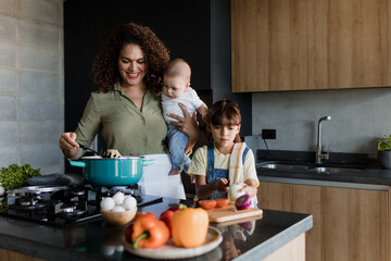 Latin single mother cooking with child daughter and baby at kitchen in Mexico Latin America,...