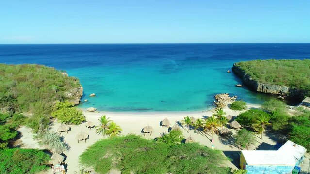 Hidden Caribbean sandy beach cove bay with beachside huts at Daaibooi beach in Curacao, aerial