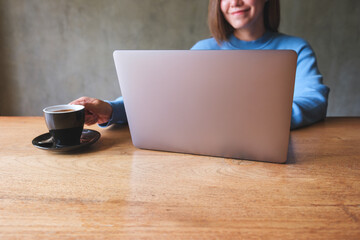 Closeup image of a young woman drinking coffee while working on laptop computer