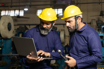 Professional indian worker or labor using laptop at factory.