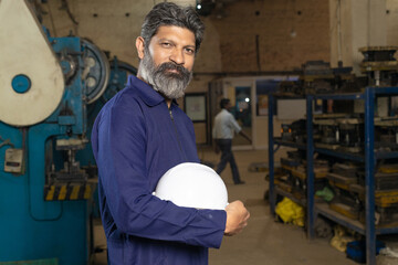 Indian worker,labor or technician standing and holding protective hard hat at factory