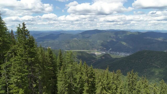 Aerial reveal town of Kellogg Idaho between pine trees from tall mountain in summer