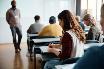 Rear view of woman writing an educational exam in classroom.