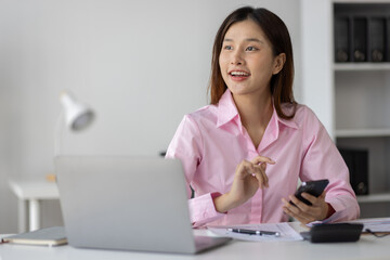 Asian businesswoman holding smartphone searching for information through website, online, surfing the internet with graph paper Work chart lying on the desk in the office