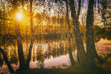 Fototapeta na wymiar Dawn on a lake or river with a sky reflected in the water, birch trees on the shore and the sunbeams breaking through them and fog in autumn. Aesthetics of vintage film.