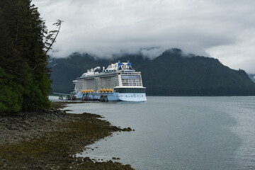 Coast bay view with modern cruiseship cruise ship liner Quantum in front of Alaska mountains on cloudy day in Hoonah, Icy Strait Point with spectacular foggy misty landscape scenery